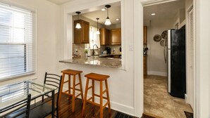 A modern kitchen with wooden cabinets, a granite countertop, and pendant lighting. There is a dining area with a glass table and two bar stools. - Downtown 2 BR Retreat / Discounts for Longer stays (Indianapolis)
