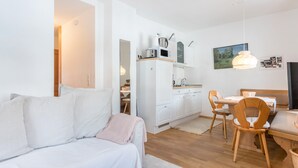 A compact living space with a bed, a dining table with chairs, a kitchenette, and a television.