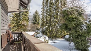 A wooden deck with a railing, snow-covered ground, and evergreen trees.