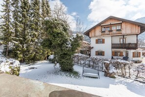 A wooden chalet with a balcony, surrounded by snow-covered trees and a clear sky.
