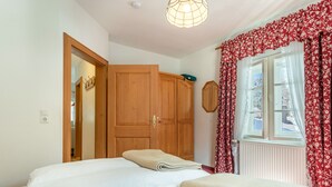 A bedroom with a bed, a wardrobe, a window with curtains, and a ceiling light fixture.