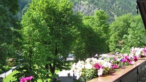 A balcony with a view of a mountain, trees, and a flower arrangement.