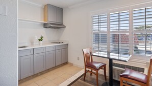 A modern kitchen with grey cabinets, a stainless steel range hood, a window with blinds, and a dining area with two wooden chairs. - Gateway Lodge (Seaside)