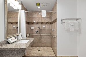 Un baño moderno con encimera de granito, un espejo grande, ducha con puerta de cristal y un perchero para toallas.