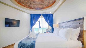 A hotel room with a large bed, a TV mounted on the wall, and a view of the beach through the window. - Esmeralda Beach Resort 2 Bedrooms Condo B 403 (Puerto Penasco)