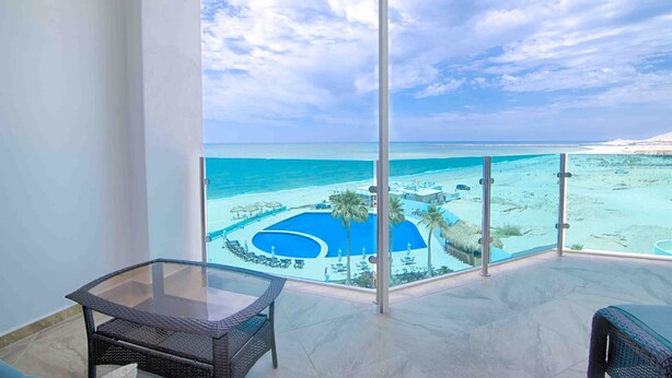 A balcony with a glass table and chairs, overlooking a pool area and beach. - Esmeralda Beach Resort 2 Bedrooms Condo B 403 (Puerto Penasco)