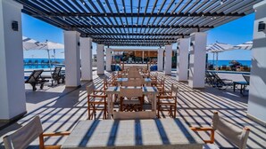A covered outdoor seating area with tables and chairs, overlooking a pool and beach. - Esmeralda Beach Resort 2 Bedrooms Condo B 403 (Puerto Penasco)