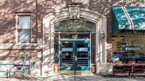 A building with a green awning, a sign for 'Black Orchid Barbers', and a 'Now Leasing' sign on the door. - The Argyle on Mass Ave (Indianapolis)