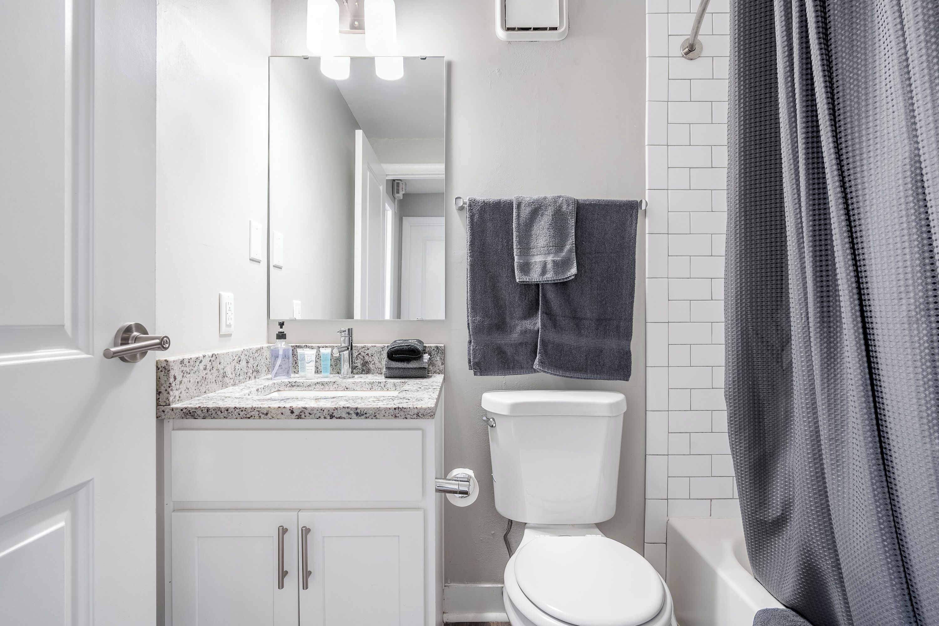 A modern bathroom with a white toilet, a granite countertop sink, a mirror, and a shower curtain.