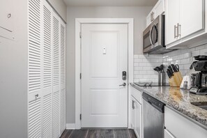 Cozinha compacta com armários brancos, micro-ondas, cafeteira e máquina de lavar louça.