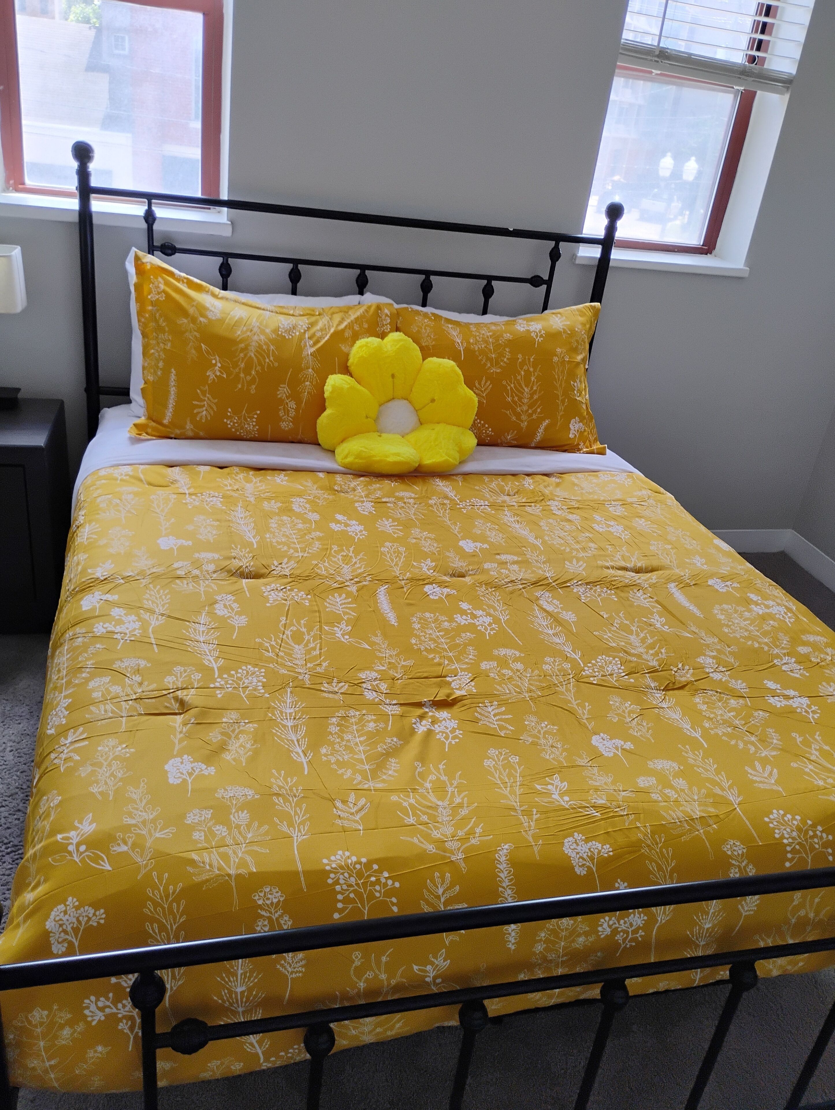 A bed with a yellow floral bedspread and a large yellow flower pillow.
