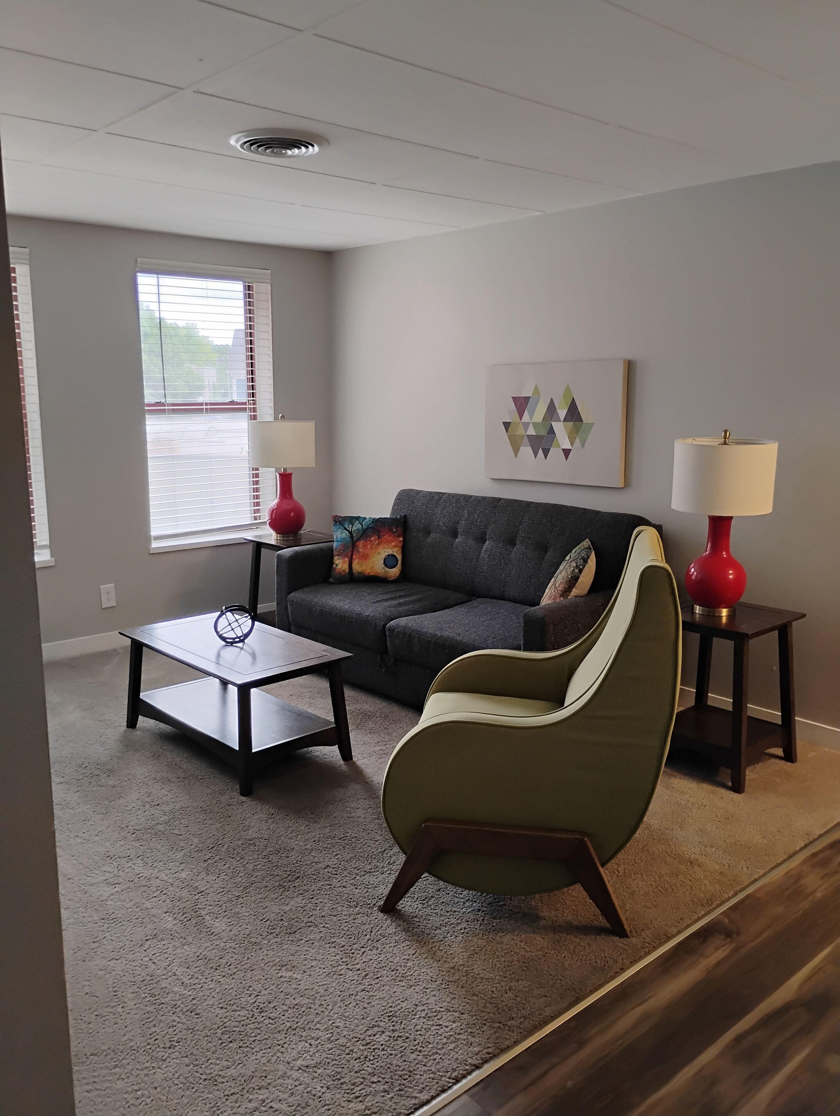 Una sala de estar con un sofá gris, un sillón verde, una mesa de centro y dos mesitas de noche con lámparas.