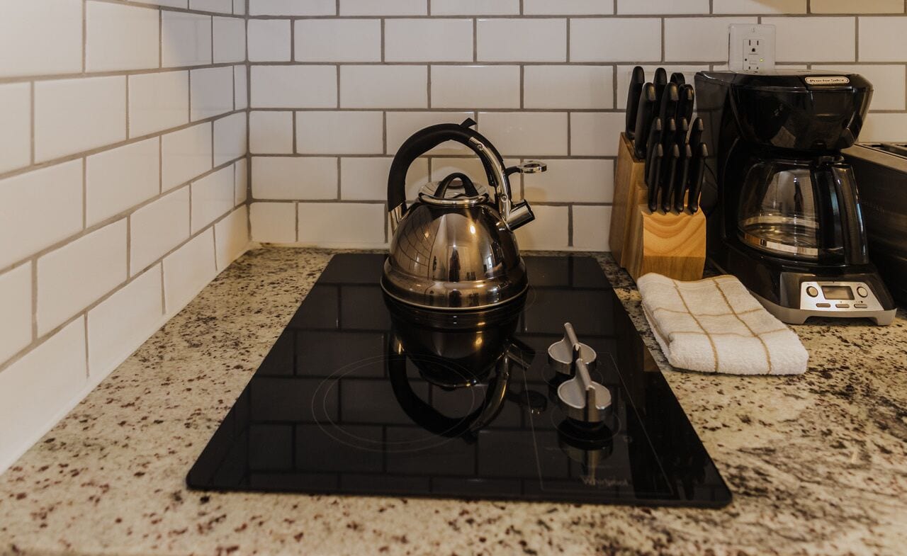 A kitchen with a black induction cooktop, a kettle, a coffee maker, and a knife block.