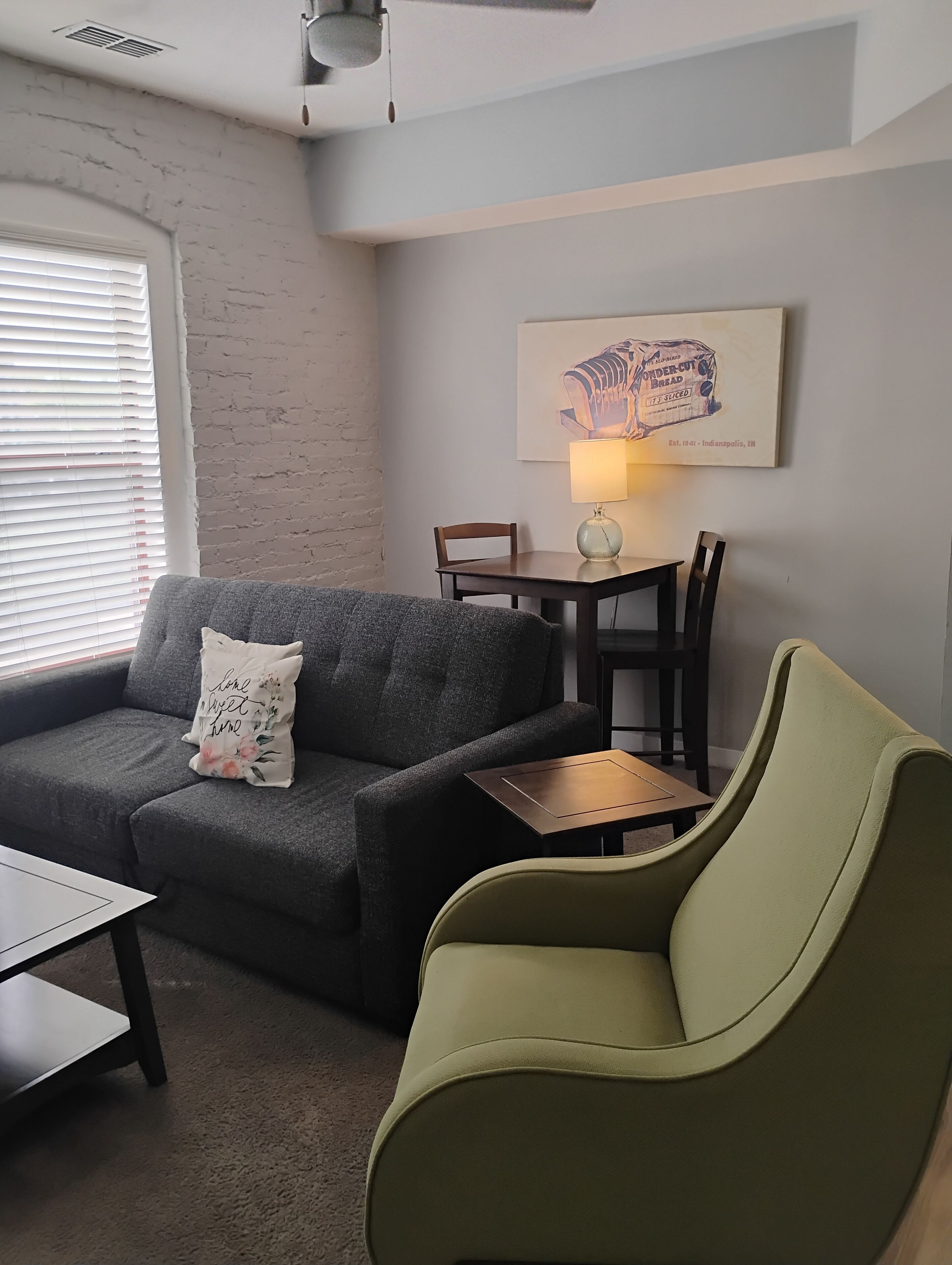 A living room with a grey sofa, a green armchair, a small table, and a wall-mounted lamp.