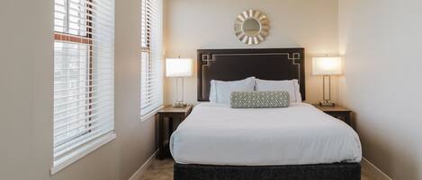 A bedroom with a large bed, two bedside tables, a wall-mounted mirror, and two floor lamps.