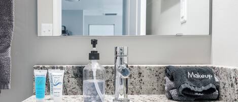 Un lavabo de salle de bain avec un miroir, un flacon de shampoing, un flacon d’après-shampoing, un flacon de thé blanc et une serviette sur laquelle est écrit le mot « Maquillage ».