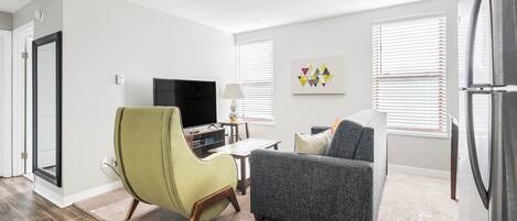 Una sala de estar moderna con un sillón verde, un sofá gris, un televisor de pantalla plana y un refrigerador.