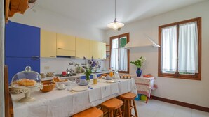 A kitchen with a dining area, featuring a table set for a meal, a hanging light fixture, and a window with curtains.