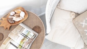 A wicker chair with a cushion, a wooden bowl with seashells, and a magazine on a woven mat.