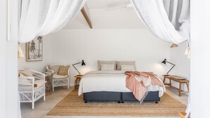 A bedroom with a bed, two bedside tables, a chair, and a hanging light fixture.