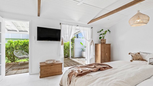 A bedroom with a bed, a TV, a wooden cabinet, and a wicker chair.