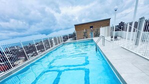 A swimming pool with a tiled pattern, surrounded by a white fence and a building in the background. - HolidayRento Bondi Rooftop Pool & Air Con Studio (Bondi)