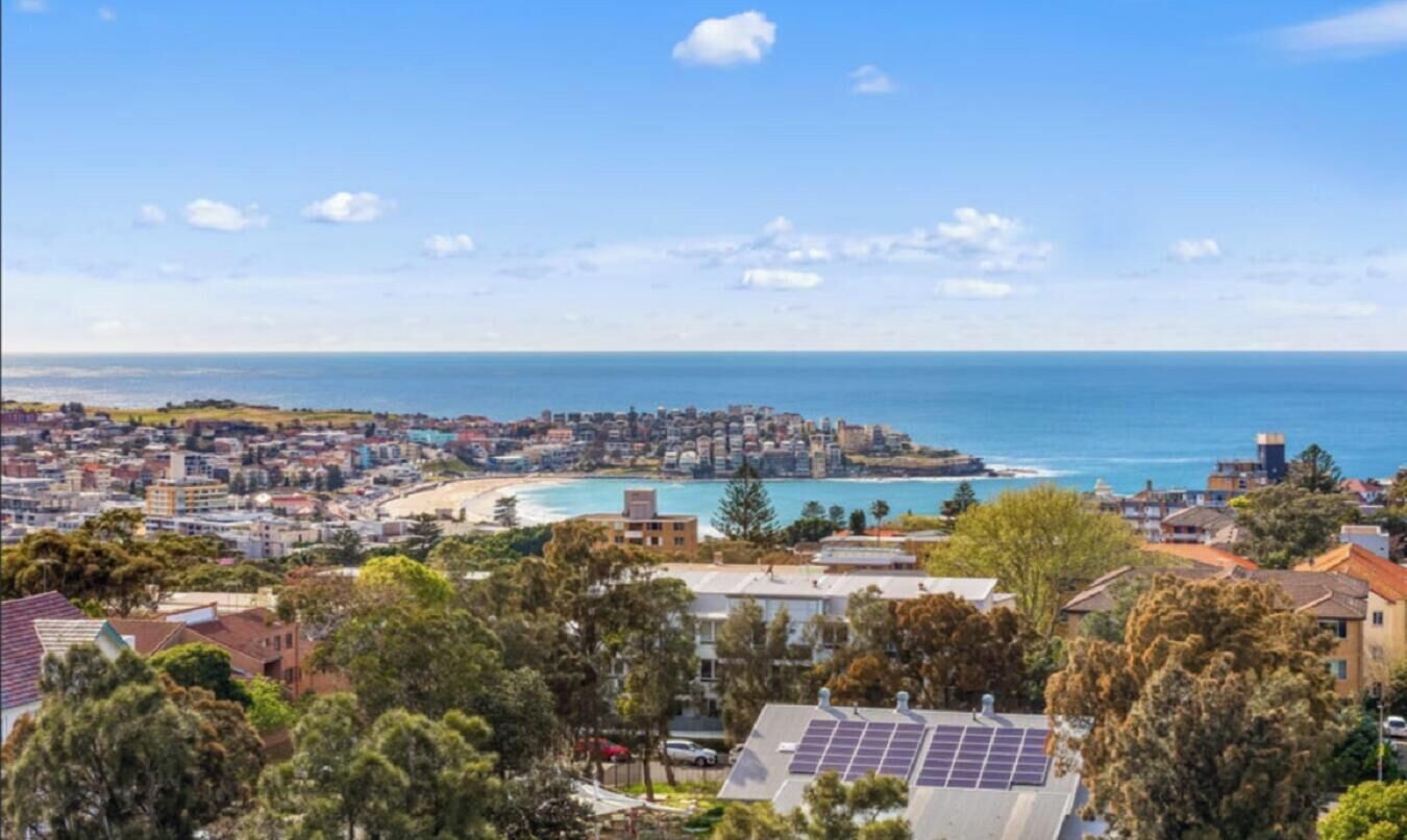 A coastal cityscape with a view from a rooftop pool, featuring a beach, ocean, and residential buildings.