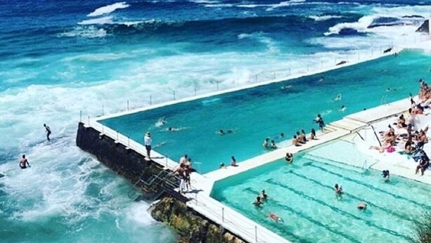 A large outdoor swimming pool with a view of the ocean, surrounded by a stone wall. - HolidayRento Bondi Rooftop Pool & Air Con Studio (Bondi)