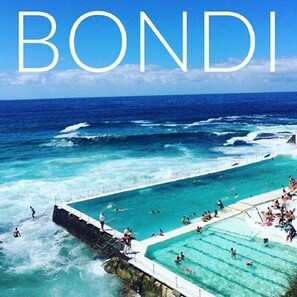 A large outdoor swimming pool with a view of the ocean, surrounded by a stone wall. - HolidayRento Bondi Rooftop Pool & Air Con Studio (Bondi)