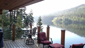 A wooden deck with a table and chairs overlooking a calm lake and forested hills.