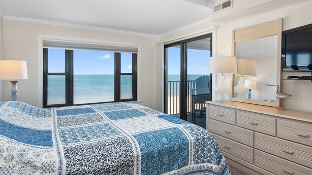 A hotel room with a large bed, a dresser, a mirror, and a view of the ocean.