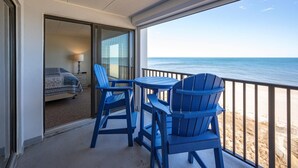 A balcony with a view of the ocean, featuring a bed, a table, and two chairs.