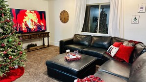 Una sala de estar con un árbol de Navidad, sofás de cuero, un televisor de pantalla plana y un reloj grande en la pared.