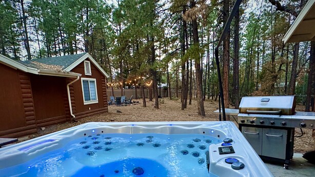 Un jacuzzi en zona boscosa con una cabaña de madera y una parrilla.