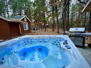 Ein Whirlpool inmitten eines bewaldeten Geländes mit einer Holzhütte und einem Grill.