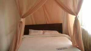 A bed with a canopy, a wooden headboard, and a pillow with a tag. - Cicada Hotel (Eldoret)