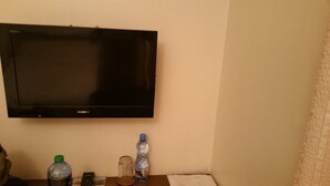 A flat-screen TV mounted on a wall, a remote control, a water bottle, and a glass on a small table. - Cicada Hotel (Eldoret)