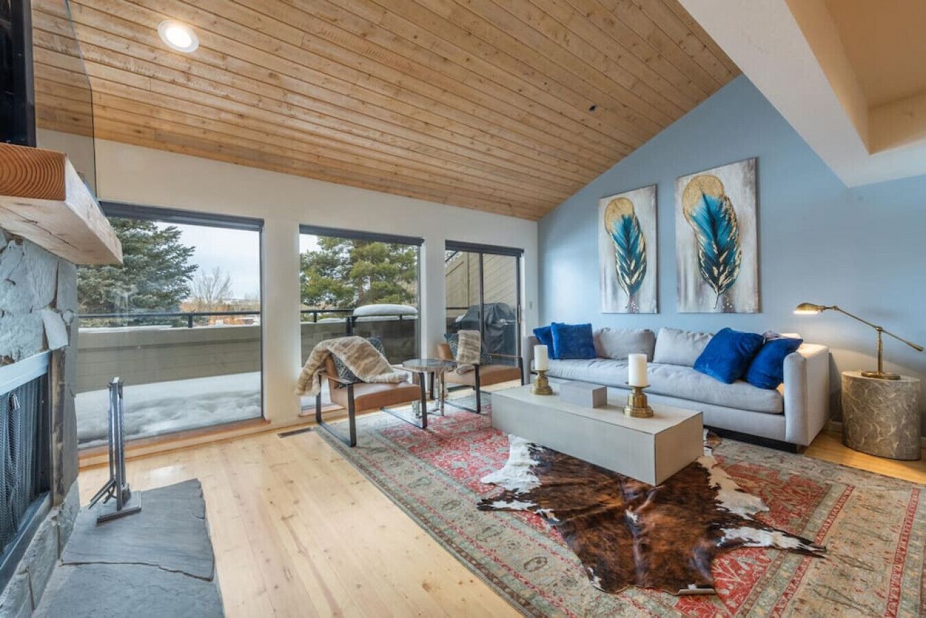 A modern living room with a stone fireplace, a large window, and a ceiling with wooden beams.