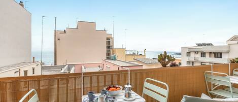 Ein Balkon mit Frühstückstisch, mit Blick auf eine Küstenlandschaft mit Gebäuden und einer Kaktuspflanze.