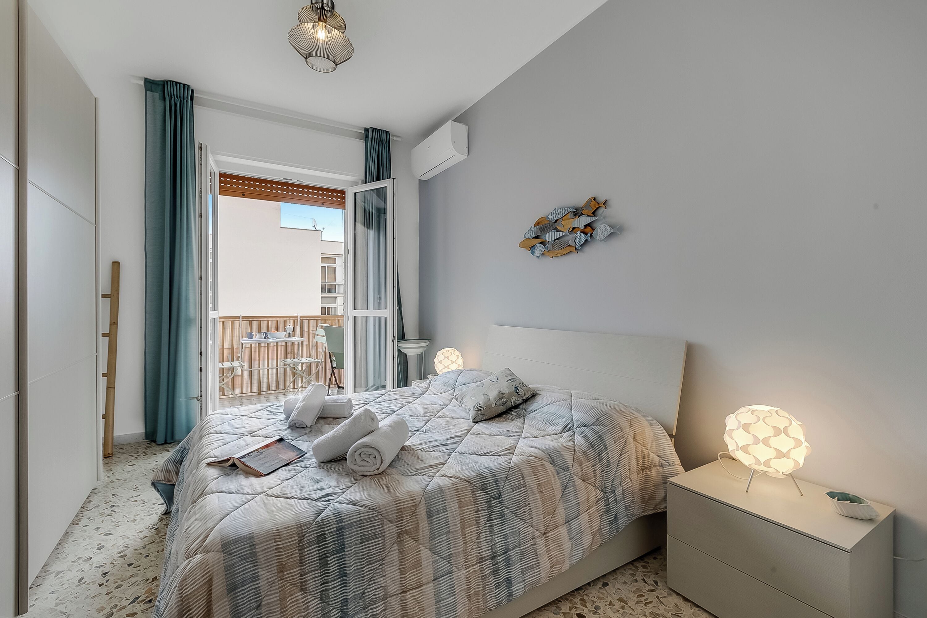 A bedroom with a bed, bedside table, and a view of an outdoor balcony.