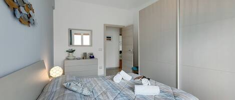 A modern bedroom with a large bed, a bedside table with a lamp, a mirror, and a wardrobe.