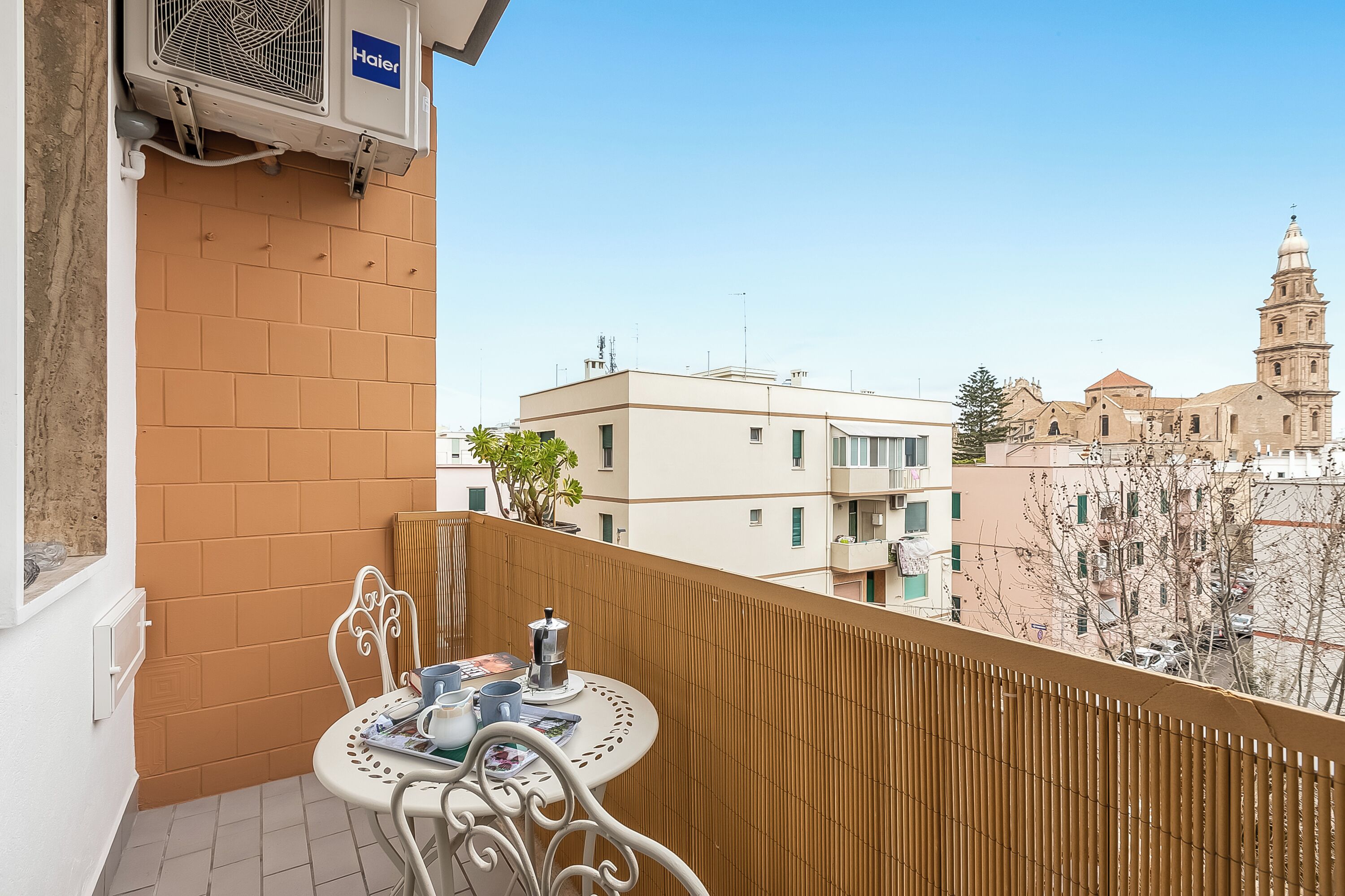 A balcony with a table and chairs, a radiator, and a view of a historic building with a bell tower.