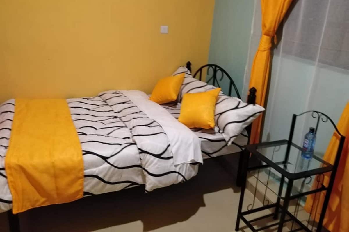 A small, single-bed room with a yellow and white striped bedspread, two yellow pillows, and a black metal chair.