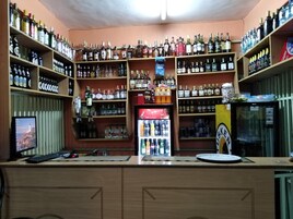 Un bar con estantes llenos de botellas de licores, un refrigerador y un monitor de computadora.