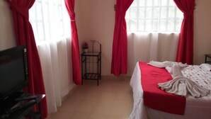 A bedroom with a bed, a TV, and a small table with a flower vase. - Sizzling Waters Resort (Nakuru)