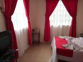 Un dormitorio con una cama, un televisor y una pequeña mesa con un jarrón.