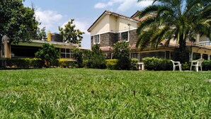 A grassy lawn with a building in the background, surrounded by trees and bushes. - Sizzling Waters Resort (Nakuru)