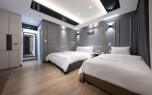 Habitación de hotel moderna con dos camas, un armario y un baño visible a través de una puerta abierta.