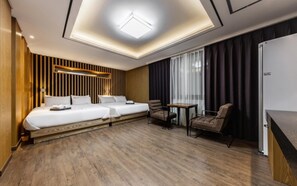 Habitación de hotel con dos camas, una mesita, una silla, un minibar y un ventanal con cortinas.