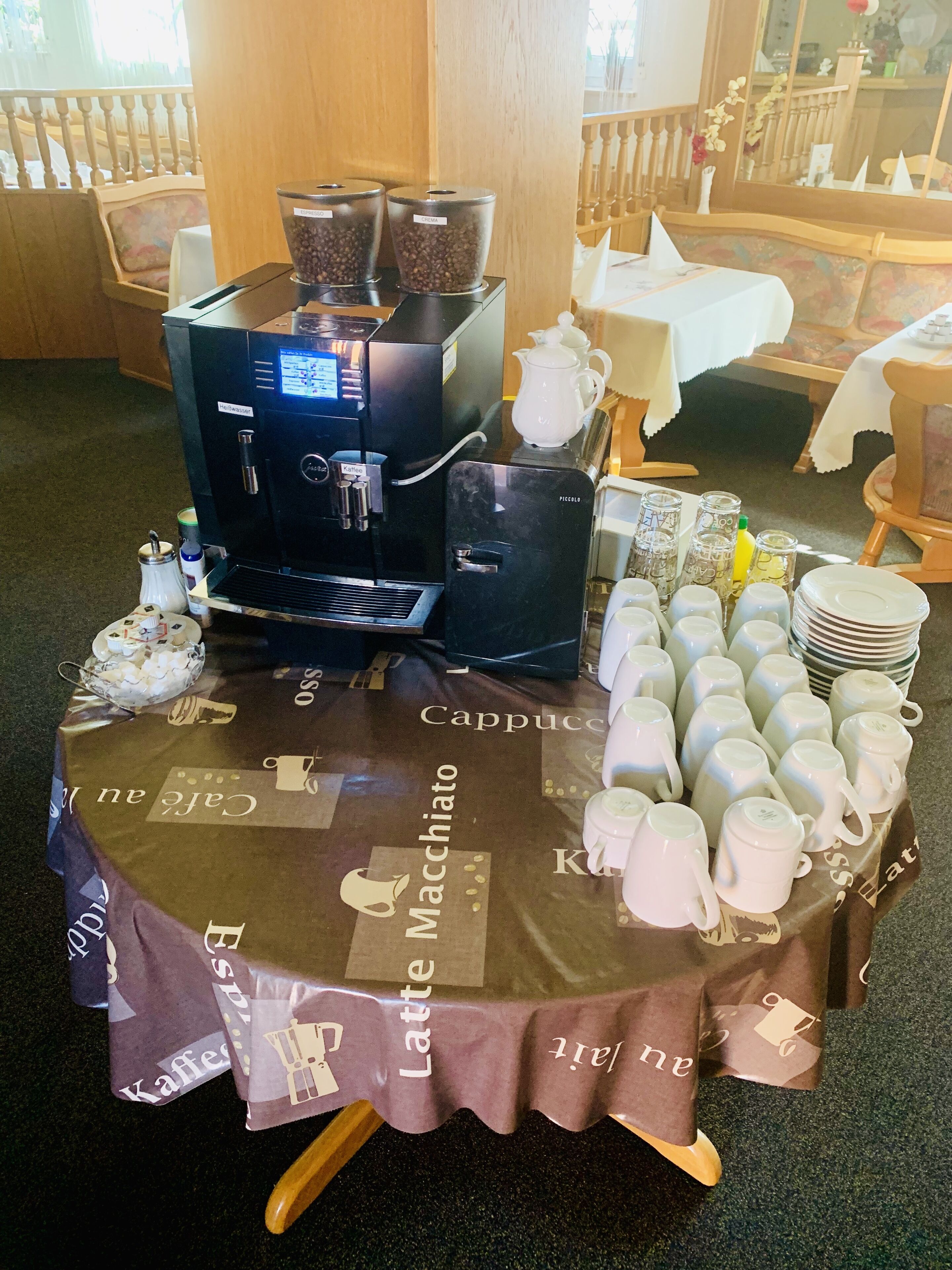 A coffee station with a coffee machine, cups, and a table covered with a branded tablecloth.